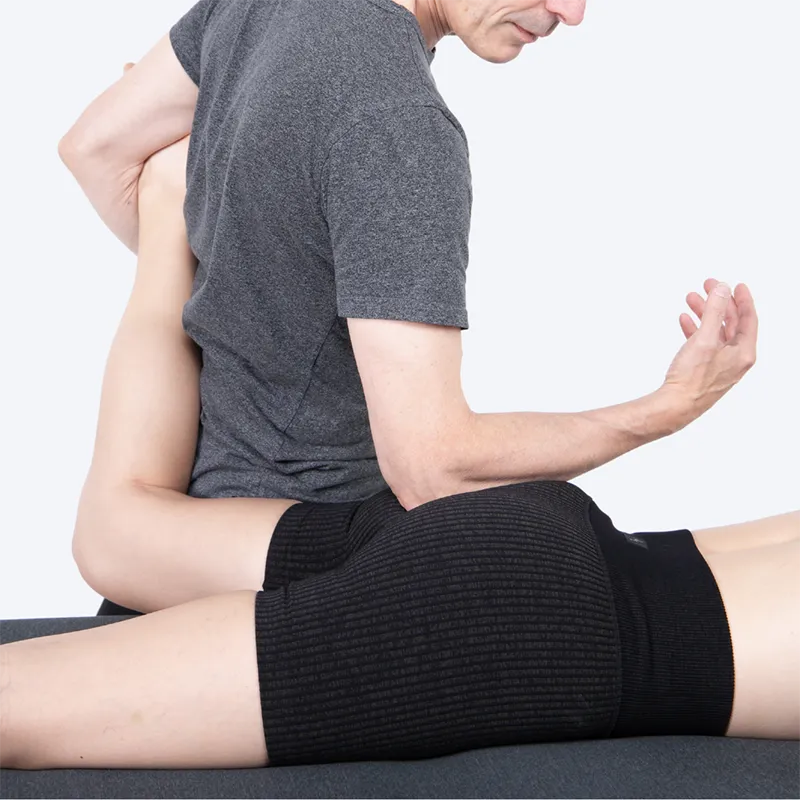 A massage therapists tends to a prone client, working on the deep six external hip rotators.