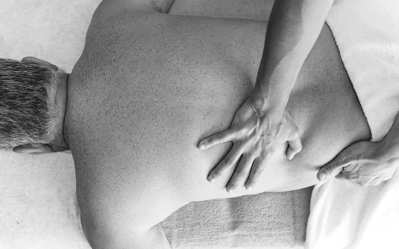 A prone client has his back and side worked on by a massage therapist.