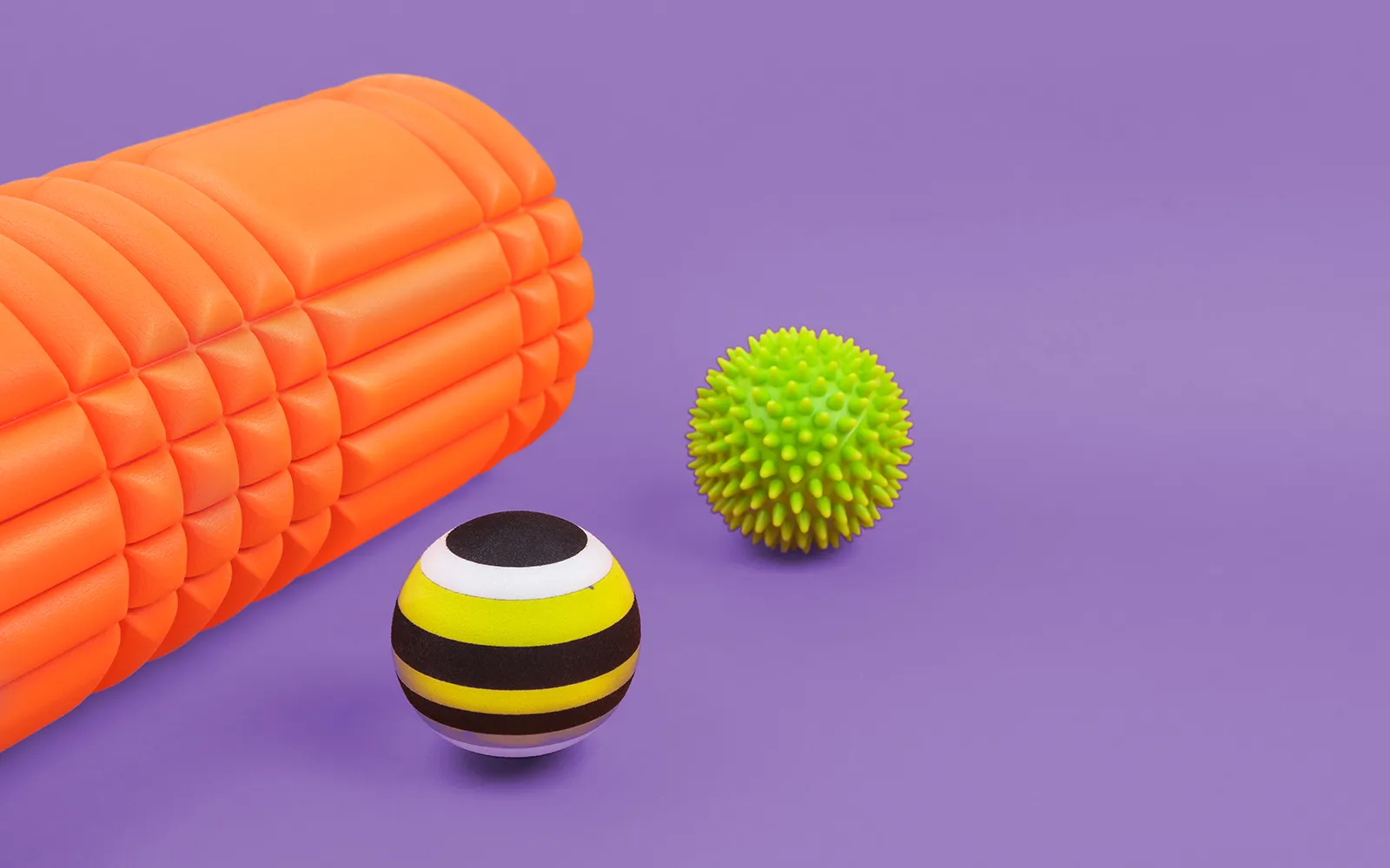 A neon orange foam roller and two different kinds of therapy balls.