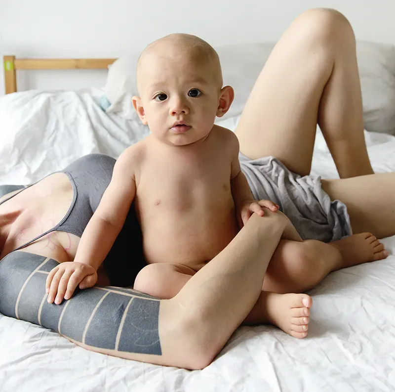 JF21_ResolvingWounds2 A young child seated with its mother lying down and holding them on the bed.